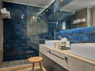 Moderne Hotelbadezimmer mit blauen Fliesen, großem Spiegel und Holzhocker.