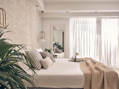 Modernes Schlafzimmer mit großem Bett, Kissen, Decke und Pflanzen neben dem Fenster mit Vorhängen