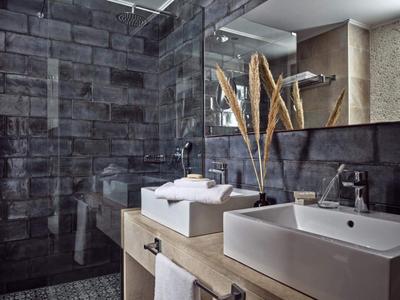 Modernes Badezimmer mit dunklen Fliesen, zwei weißen Waschbecken und dekorativen Pflanzen