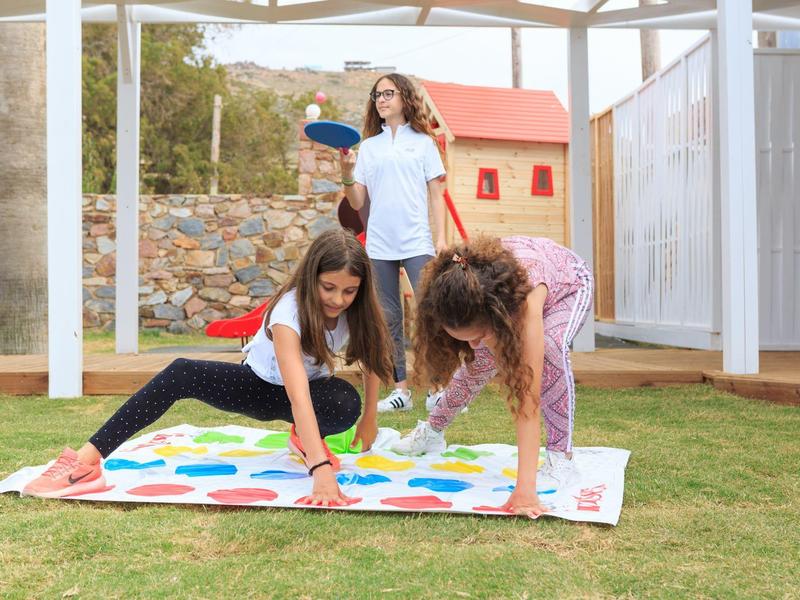 Drei Mädchen spielen Twister auf einer Matte im Garten bei Sonnenschein.