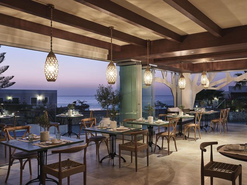 Offenes Restaurant mit Holzmöbeln, Lampen, Blick auf Meer und Dämmerungshimmel.