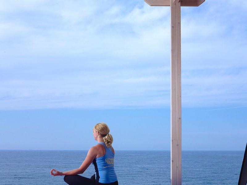 Moderner Barbereich mit Marmorfront, weißen Barhockern und Meerblick durch große Fenster.