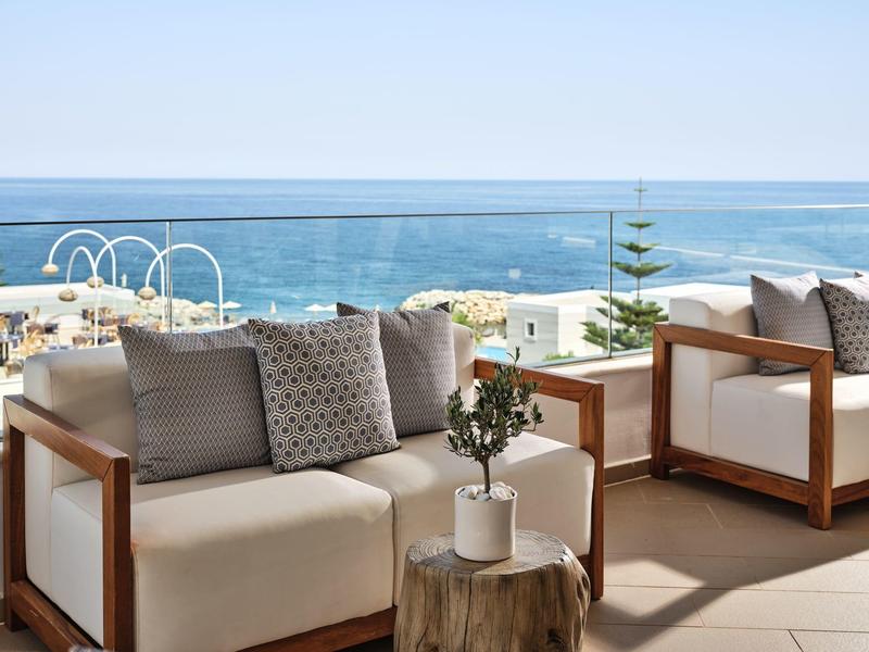 Terrasse mit bequemen weißen Sesseln, Kissen und kleinem Tisch vor klarem Meerblick.