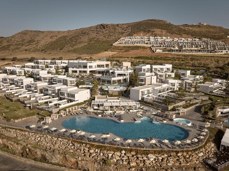 Große Ferienanlage mit weißen Gebäuden, mehreren Pools und umgeben von braunen Hügeln.