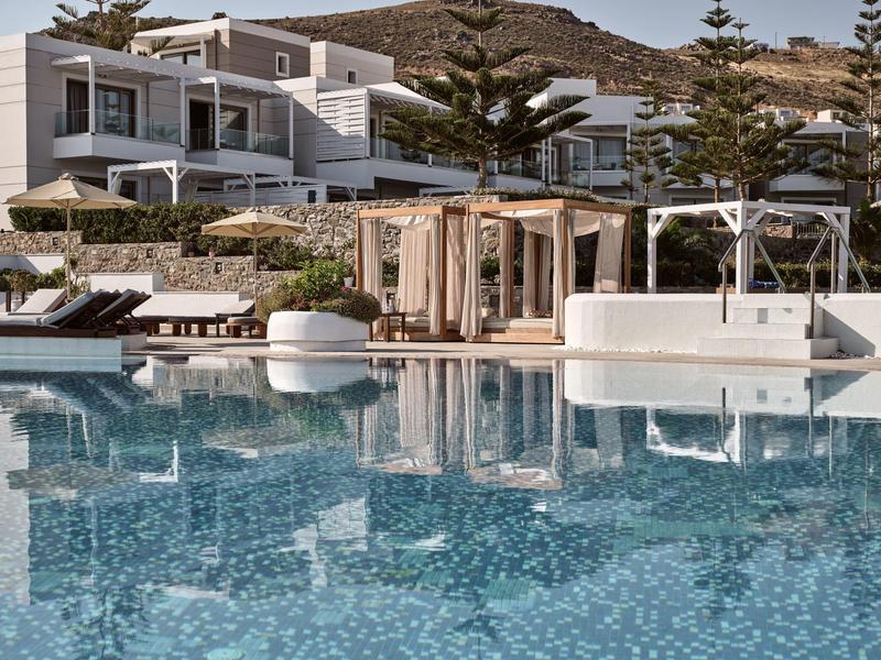 Moderner Poolbereich mit Liegen, Pavillons und weißen Gebäuden im Hintergrund unter blauem Himmel.