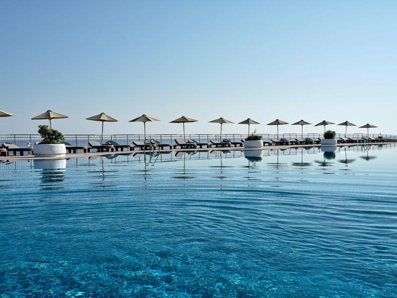 Großer Pool mit klarem blauem Wasser, Reihen von Sonnenliegen und Sonnenschirmen am Rand.