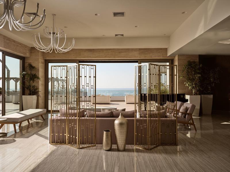 Moderner Wohnraum mit großen Fenstern, hellem Marmorboden und Blick auf das Meer bei Tageslicht.