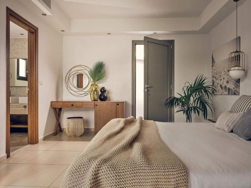 Gemütliches Schlafzimmer mit modernem Dekor, Holzkommode, Pflanzen und Blick ins Badezimmer.