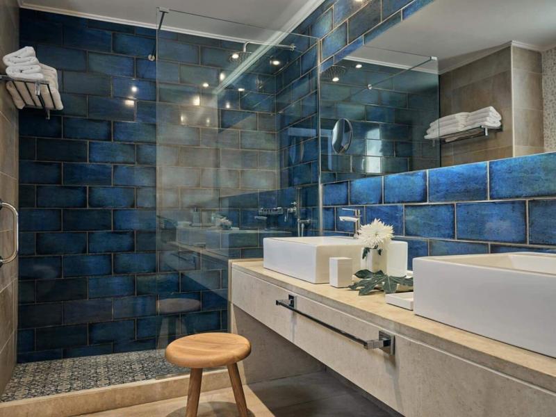 Moderne Hotelbadezimmer mit blauen Fliesen, großem Spiegel und Holzhocker.