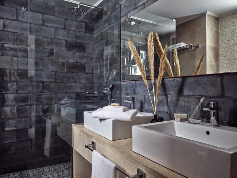 Modernes Badezimmer mit dunklen Fliesen, zwei weißen Waschbecken und dekorativen Pflanzen