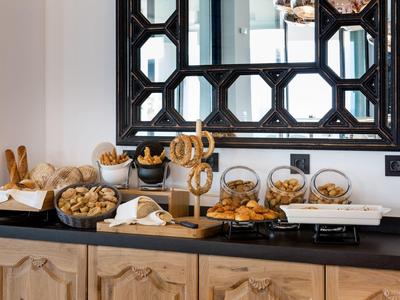 Buffet met gebak en brood onder een grote geometrische spiegel op een houten kast.