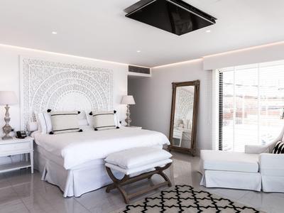 Lichte hotelkamer met groot bed, decoratieve witte muur, bankje, fauteuil en grote spiegel.