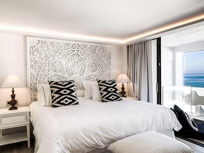 Lichte hotelkamer met groot wit bed, decoratieve kussens en balkon met uitzicht op de oceaan.