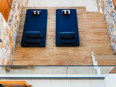 Moderne hotelpatio met twee blauwe ligstoelen onder een helder zwembad en stenen muren.