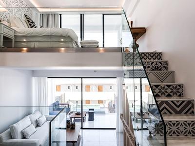 Modern loft met patroon trap, glazen balustrades en lichte woonkamer met balkon.