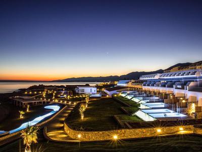 Luxe resort bij zonsondergang met verlichte paden en witte gebouwen langs de kust.