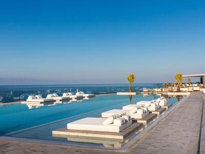 Luxe infinity pool met witte ligbedden met uitzicht op de oceaan en de heldere blauwe lucht.