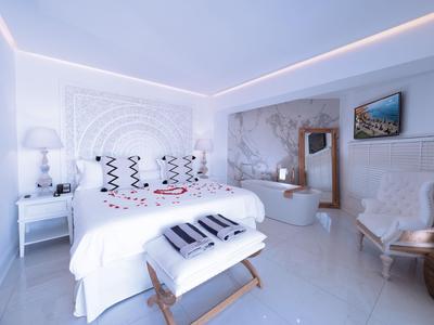 Modernes Schlafzimmer mit großem Bett, weißen Möbeln und freistehender Badewanne.