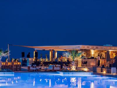 Terrasse d'hôtel en soirée avec piscine illuminée et coins salons confortables sous un ciel nocturne clair.