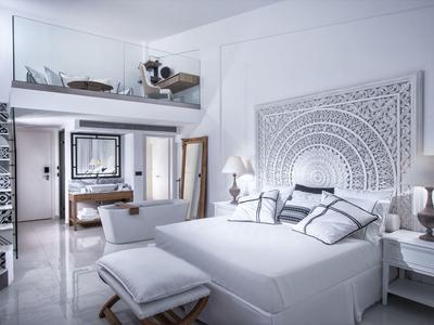 Licht hotelkamer met witte inrichting, groot bed, gedetailleerd hoofdeinde en zitgedeelte.