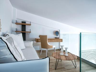 Moderne woonkamer met witte bank, houten salontafel en bureau onder een schuin plafond.