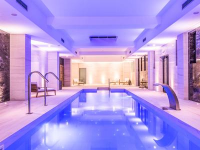 Overdekt hotelzwembad met blauwe verlichting, strak design en ligstoelen.