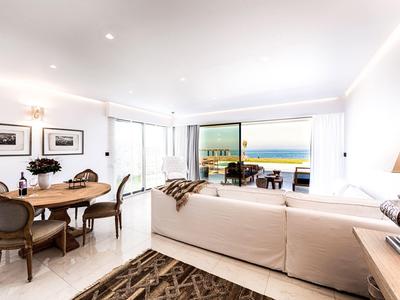 Lichte, moderne woon- en eetkamer met zeezicht, wit meubilair en grote glazen schuifdeuren.