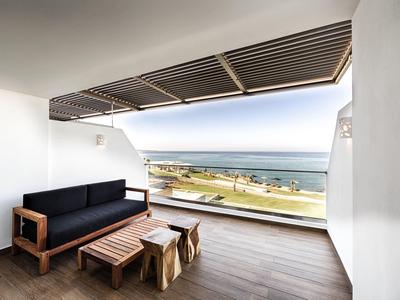 Ruim balkon met houten meubels met uitzicht op strand en oceaan onder heldere lucht.