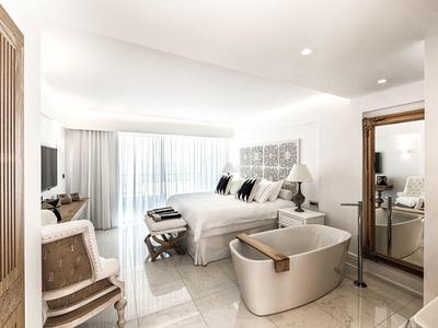 Lichte hotelkamer met groot bed, stijlvolle inrichting, stoel en een kleine zithoek bij het raam.