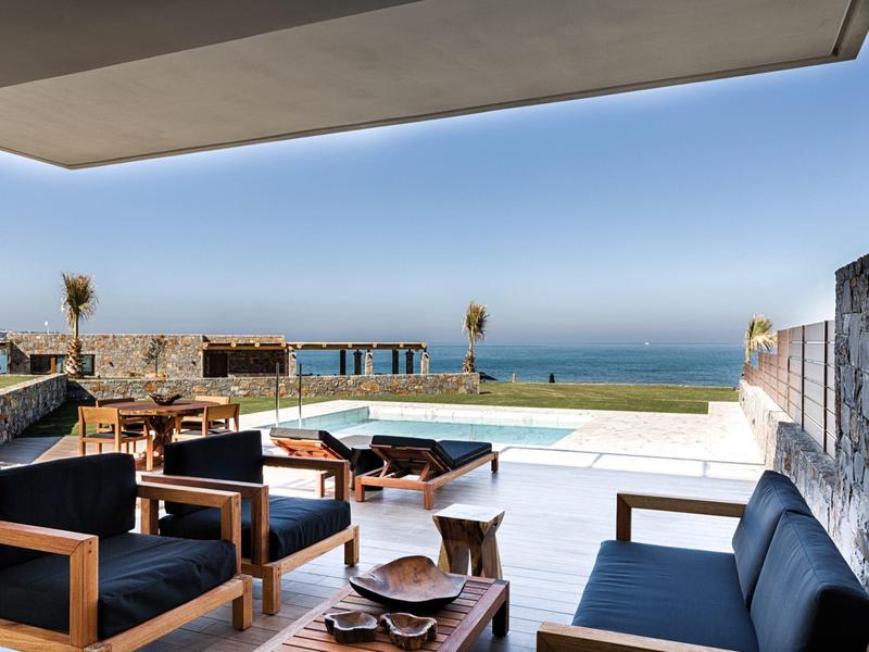 Moderne buitenzitplek met houten meubels en uitzicht op zee bij luxe hotelterras.