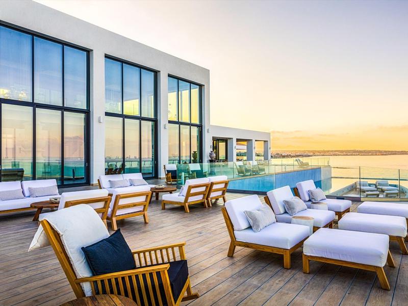 Zonsondergang met uitzicht op een modern hotelterras met loungebanken en een zwembad.