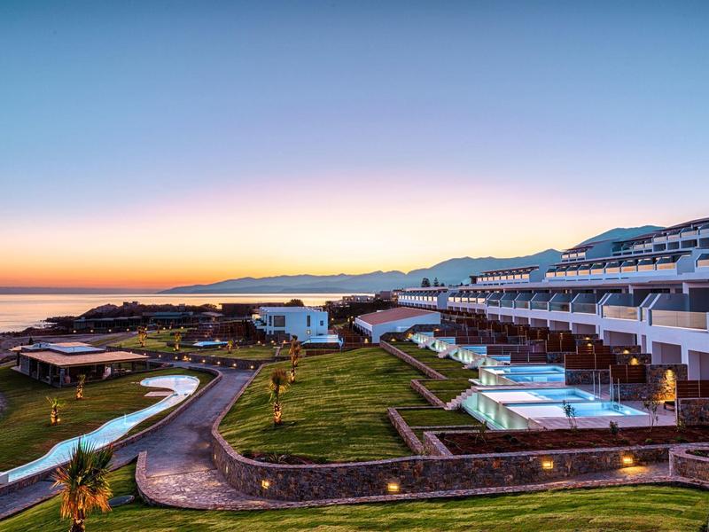 Kustresort met groene gazons, zwembaden en terrassen onder een heldere schemerlucht.