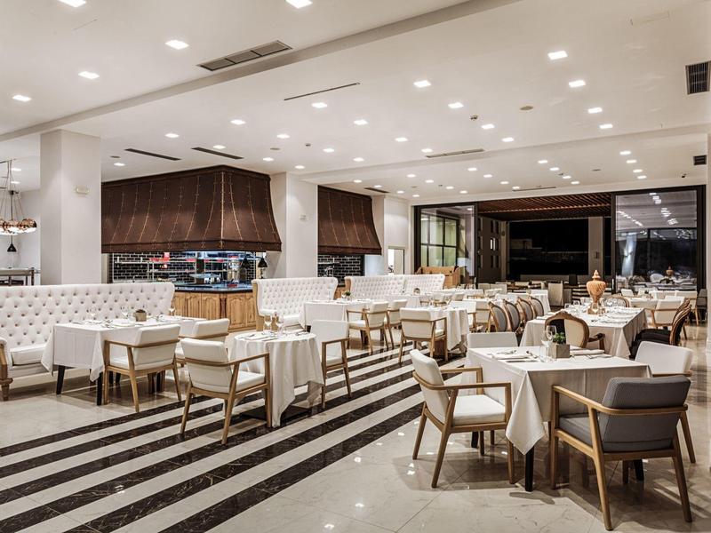 Moderne hotel eetzaal met witte tafelkleden, beklede stoelen en gestreepte vloertegels.