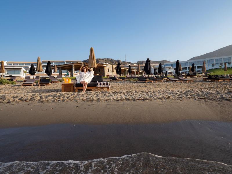 Zandstrand met lege ligbedden en parasols onder een helderblauwe lucht nabij water.