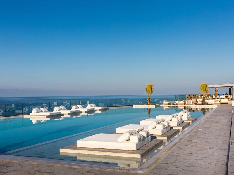 Luxe infinity pool met witte ligbedden met uitzicht op de oceaan en de heldere blauwe lucht.