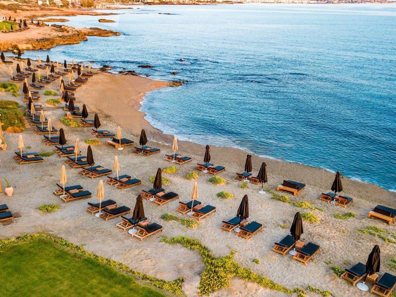 Strandresort met ligbedden en parasols langs een zandstrand naast een kalme zee.
