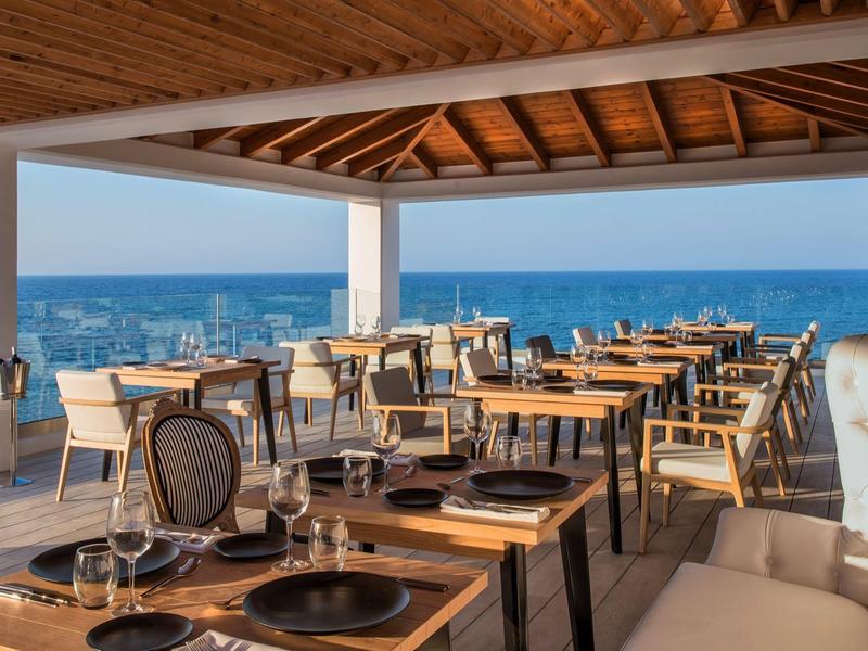 Openluchtrestaurant met houten tafels, stoelen en uitzicht op de oceaan onder een houten dak.