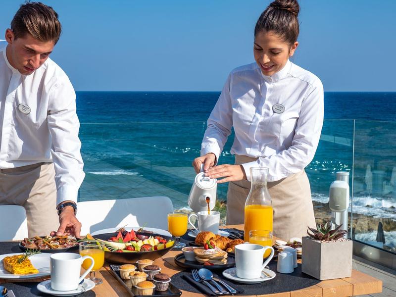 Twee obers serveren ontbijt drankjes en gerechten met uitzicht op de oceaan.