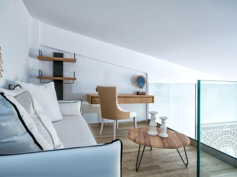 Moderne woonkamer met witte bank, houten salontafel en bureau onder een schuin plafond.