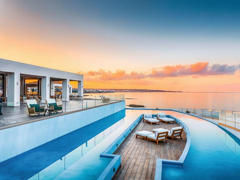 Moderne infinity pool met uitzicht op zonsondergang en oceaan, met ligstoelen en terras.