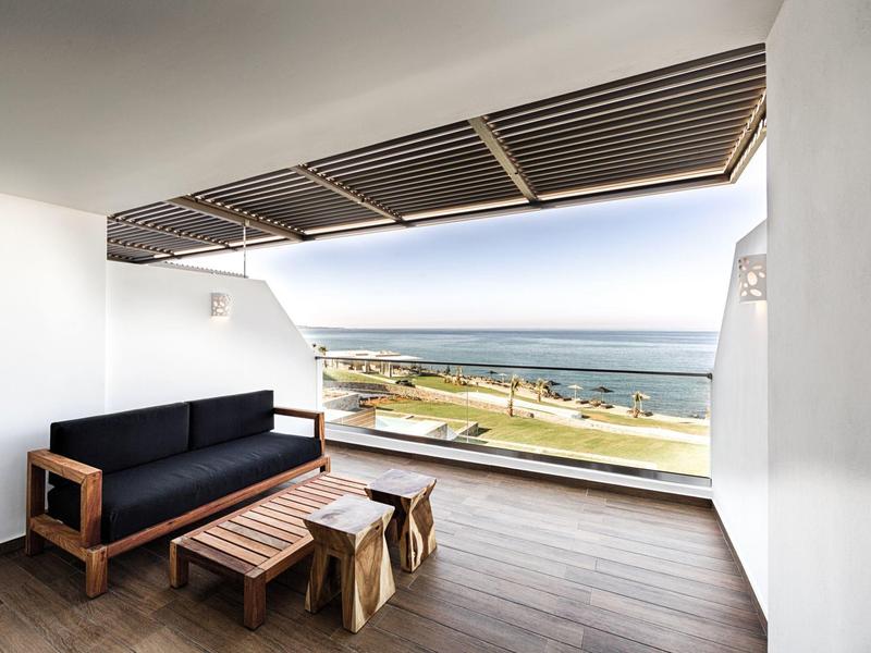 Ruim balkon met houten meubels met uitzicht op strand en oceaan onder heldere lucht.