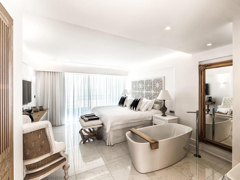 Lichte hotelkamer met groot bed, stijlvolle inrichting, stoel en een kleine zithoek bij het raam.