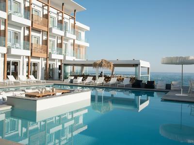 Modern hotelzwembad met ligstoelen en uitzicht op zee op een zonnige dag.