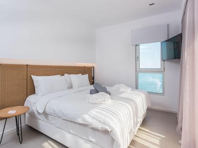 Moderne, lichte slaapkamer met tweepersoonsbed, raam en klein bijzettafeltje.