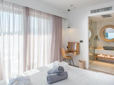 Lichte hotelkamer met groot raam, bureau en moderne badkamer met spiegel.