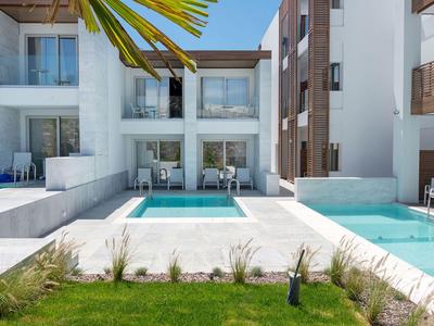 Piscina moderna dell'hotel con lettini e ringhiere in vetro davanti a edifici bianchi.
