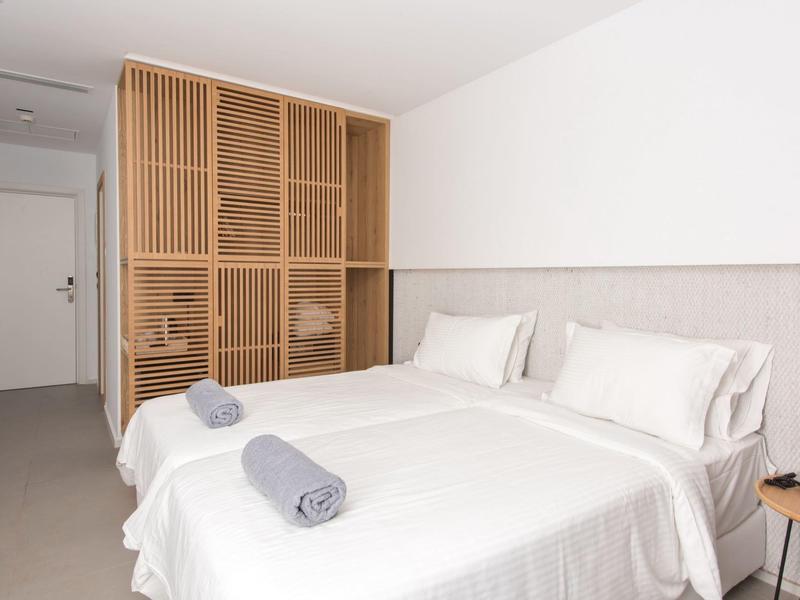 Moderne hotelkamer met tweepersoonsbed, wit beddengoed en houten kast aan de muur.