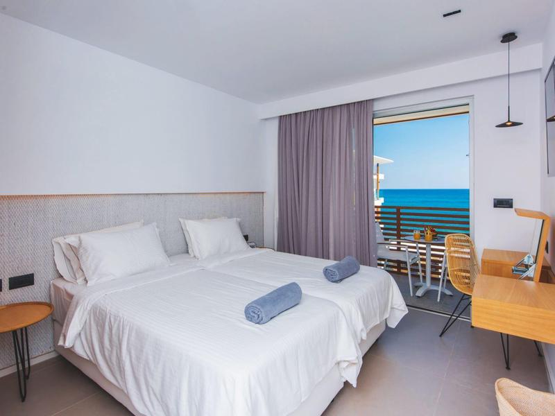 Modern hotelkamer met twee eenpersoonsbedden, tafel, balkon en uitzicht op zee.