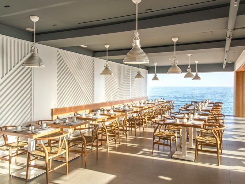 Lichte, moderne eetzaal met houten stoelen en uitzicht op zee.