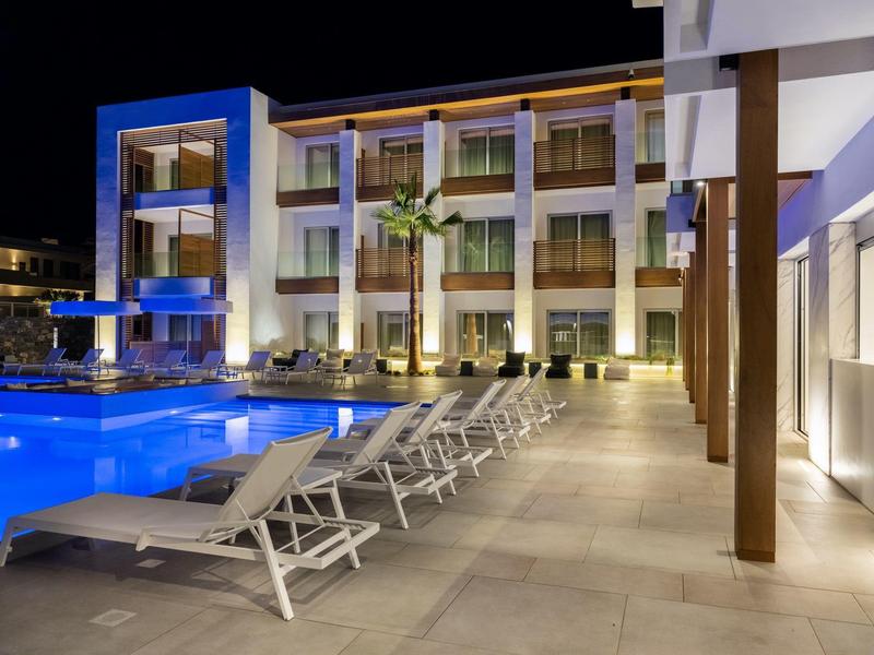 Moderne hotelbinnenplaats met verlicht zwembad en witte ligbedden in de nacht.